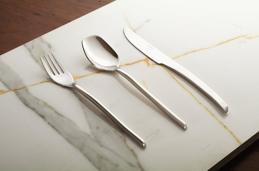 Stainless steel silverware set including knife, fork, spoon, and teaspoon on a reflective surface.